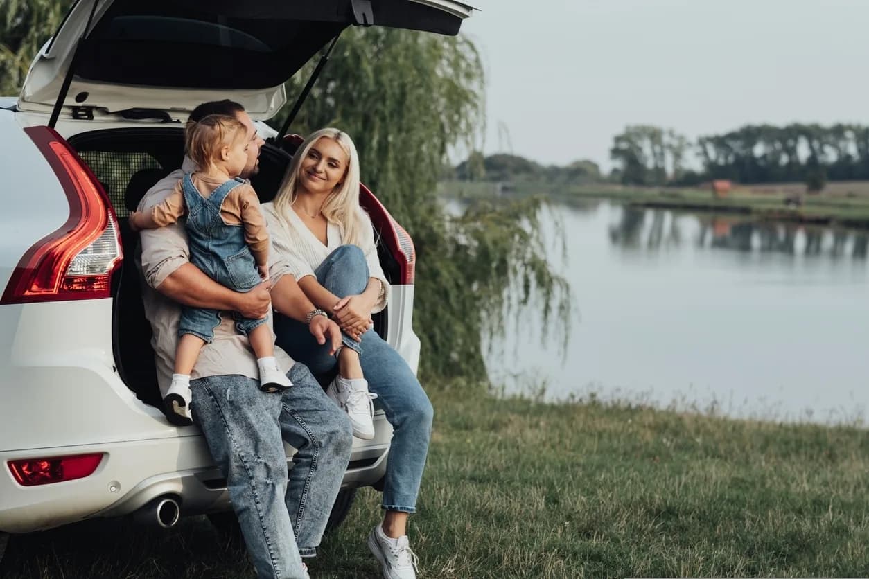 Young family of 3 sitting in car boot enjoying the lake