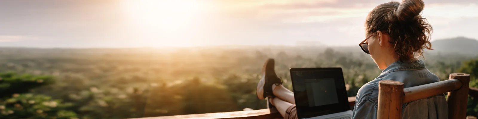 Woman sitting on balcony over looking forest working on laptop